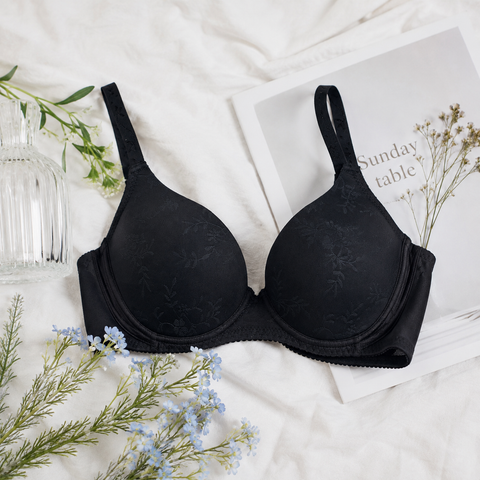 Black Wacoal underwired bra laid flat on white bedlinen with dried flowers